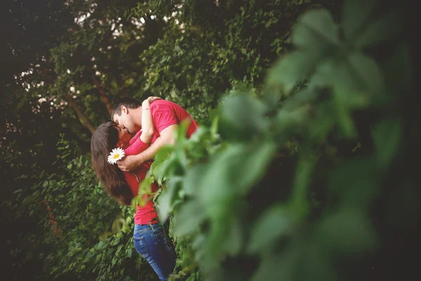 Der Kerl küsst das Mädchen. Beide tragen Rothemden. Sie teilten sich einen Zaun und Pflanzen.. — Stockfoto