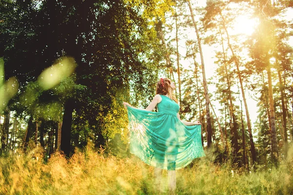 Schöne junge Frau in elegantem hellgrünem Kleid, die im Wald steht, mit Sonnenstrahlen, die durch die Blätter der Bäume strahlen. Weicher Fokus und straffende Wirkung — Stockfoto