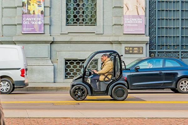 Milão, Itália - 19 de outubro de 2015: mini carro elétrico para dois passeios nas ruas de Milão, na Itália. Atrás do volante de um homem de capa de chuva e uma mulher ao seu lado . — Fotografia de Stock