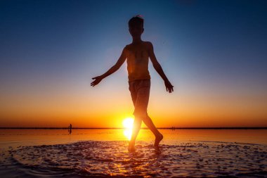 Günbatımının arka planında pembe bir tuz gölünde çıplak ayaklı bir çocuk.