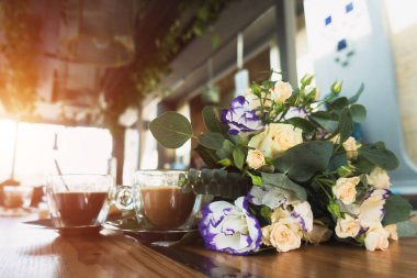 Bir buket çiçek ve masada iki fincan kahve.