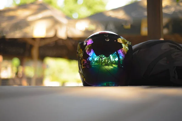 A motorcycle helmet with a mirror visor lies on the table with a backpack for travel.