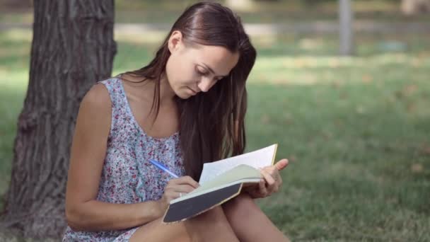 Mladá žena píše ve svém deníku v parku — Stock video