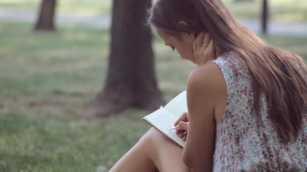 Молода жінка пише у своєму щоденнику в парку — стокове відео