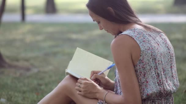 Mujer joven escribe en su diario en el parque — Vídeo de stock