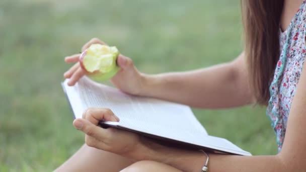 Jovem mulher lendo livro e comer maçã no parque . — Vídeo de Stock