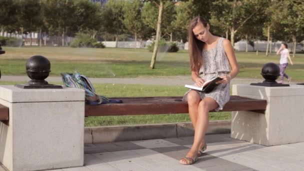 Mujer joven sentada en el banco con un libro — Vídeo de stock