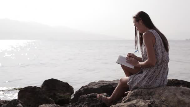 Yong kobieta robiąc notatki w dzienniku na plaży — Wideo stockowe