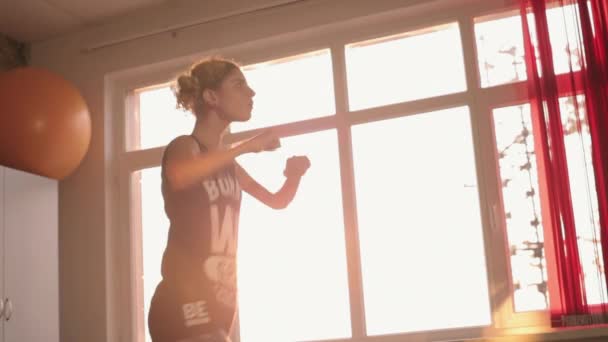 Молода мила дівчина танцює біля вікна на заході сонця — стокове відео