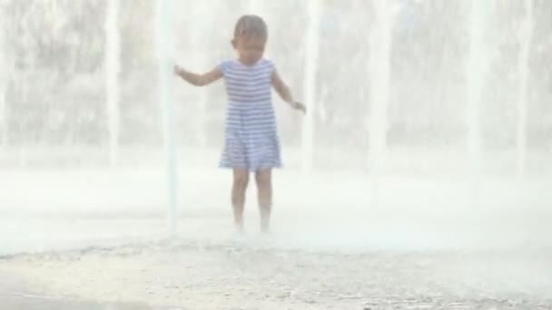 Милая девочка бежит через фонтан и смеется — стоковое видео