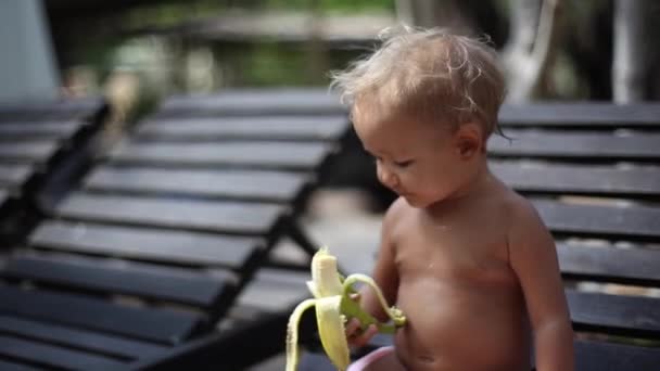 Pequeña linda chica come un plátano al aire libre — Vídeo de stock