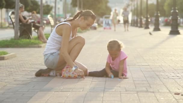 Menina bonito e sua mãe desenho com giz na calçada — Vídeo de Stock