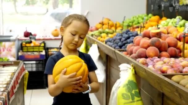 Niña con melón maduro está caminando a lo largo de las filas de comestibles hacia el cajero — Vídeos de Stock