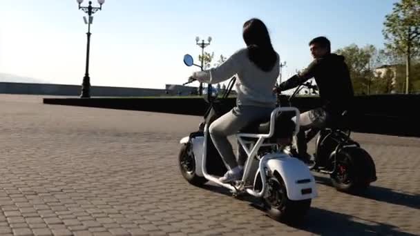 Happy couple on electric scooters are riding through urban seafront at morning — Stock Video