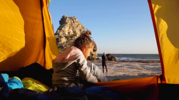 Child girl is puts her shoes while sits in camping tent at beautiful beach — Stock Video