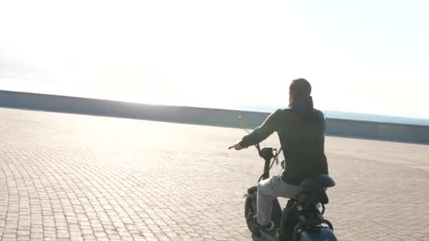 Masculino em scooter elétrico está montando em frente ao mar urbano na manhã ensolarada — Vídeo de Stock