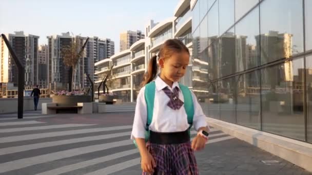 Μικρή μαθήτρια με σχολική στολή πηγαίνει στο σχολείο στο τοπίο της πόλης — Αρχείο Βίντεο