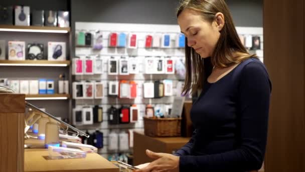 Giovane donna sceglie un nuovo smartphone in un negozio di elettronica. — Video Stock