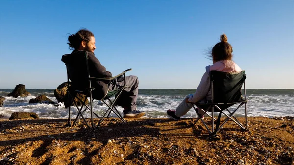 Padre con hija pequeña se sienta en sillas en la playa, vista trasera. — Foto de Stock