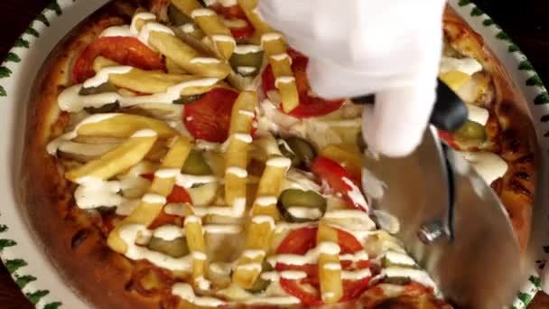 Рука режет пиццу с картошкой фри на ломтики с помощью резака для пиццы. — стоковое видео
