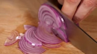 Eller kırmızı soğanı tahta tahtada bıçakla kesiyor, yakın plan.