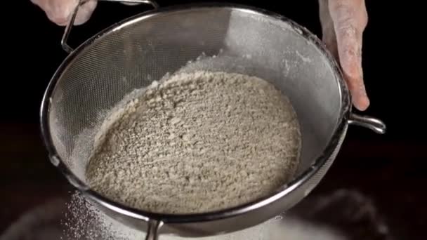 Zbliżenie białej mąki spada przez sito stalowe na czarnym tle — Wideo stockowe