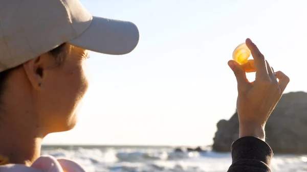 Mujer joven está sosteniendo concha en la mano y mirando el sol a través de la cáscara Imágenes De Stock Sin Royalties Gratis