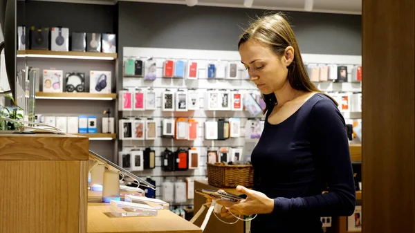 Mujer joven elige un nuevo smartphone en una tienda de electrónica. Fotos De Stock