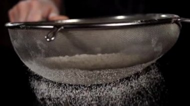 Beyaz un yakın plan siyah zemin üzerindeki çelik eleğe düşüyor.