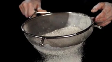 Beyaz un yakın plan siyah zemin üzerindeki çelik eleğe düşüyor.