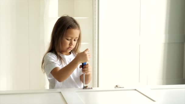 Küçük bir kız çocuğu dolabın kapısına menteşeleri yerleştiriyor. — Stok video