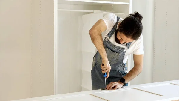 Un uomo sta installando le cerniere sulle porte dell'armadio Immagine Stock