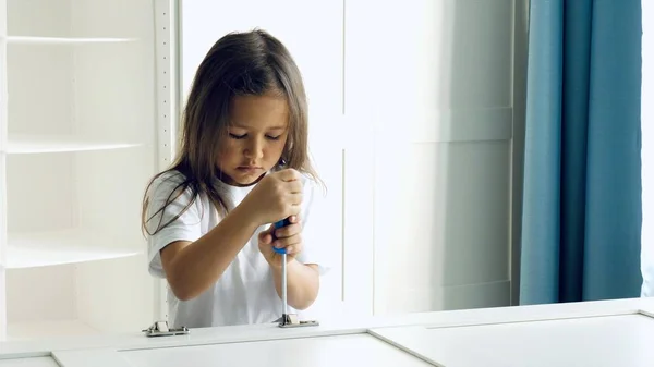 O fetiță instalează balamalele pe ușile dulapului Imagini stoc fără drepturi de autor