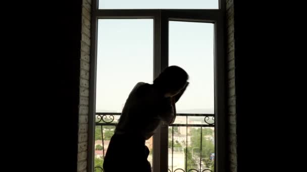 若い女性のシルエットはバルコニーへの扉の窓を掃除している. — ストック動画