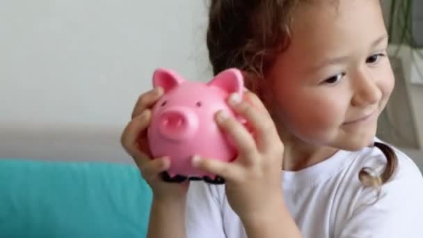 Smiling child girl is shaking piggy bank — Stock Video