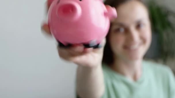 Jovem feliz está sorrindo e sacudindo rosa porquinho banco — Vídeo de Stock