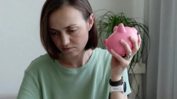 Mladá smutná žena se třese prázdným prasátkem banky — Stock video