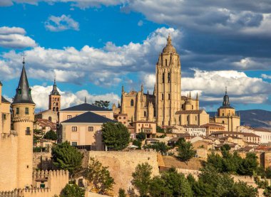 Segovia Katedrali ve kulesi ön planda Alcazar Sarayı ve şehir duvarları ve mavi gökyüzünde bulutlar ile birlikte görülüyor. İspanya