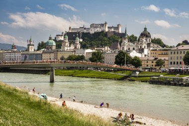 Salzburg, Avusturya, 06.11.2025: Salzach nehrinin kıyısından Marko Feingold Steg köprüsü, katedral ve şato arka planda ve kıyıda insanlar ile eski kentin görüntüsü