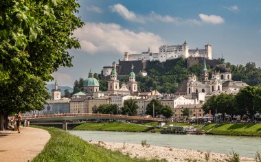 Salzburg, Avusturya, 06.11.2025: Salzach Nehri 'nden Marko Feingold Steg köprüsü, arka planda katedral ve kale ve nehir kıyısında koşan adamla birlikte eski kentin manzarası