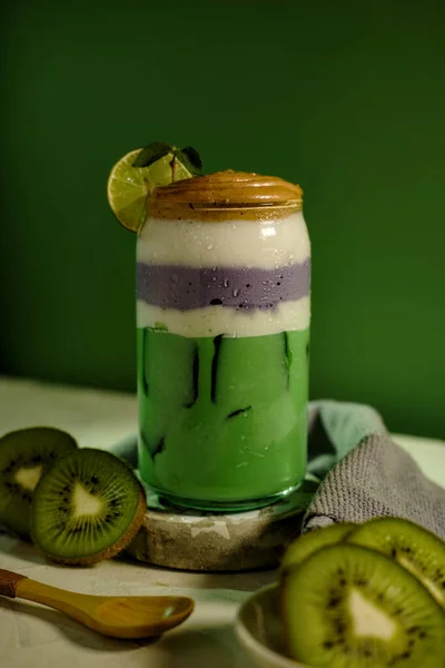 Healthy green and purple layered smoothie with kiwi slices, lime, and mint leaves for summer vibes.