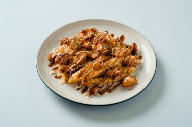 Üzerine mayonez, mozzarella ve peynir konmuş kızarmış patates, beyaz bir tabakta servis edilir..