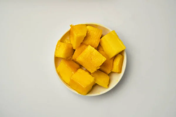 Beyaz arka planı olan küçük bir tabakta bir parça mango meyvesinin düz uzanmış hali..