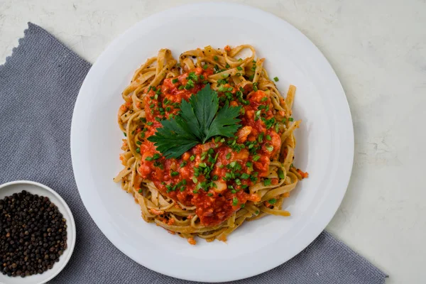 Domates soslu bir tabak spagetti ve yanında da gri bir peçetede küçük bir tabak siyah biber.