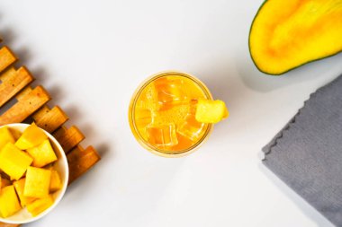 Bir bardak mango suyu veya bir dilim mango meyvesi ve gri peçeteli smoothie. Vitamin zengini içecek konseptleri