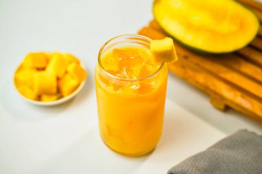 Bardakta yüksek açılı mango suyu ve arka planda mango parçaları olan buz küpleri.