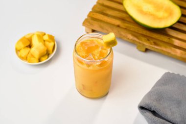 Mango suyu, beyaz arka planda mango dilimleri, gri peçeteler ve ahşap tepsilerle üst açıdan alınmış buz küpleri..