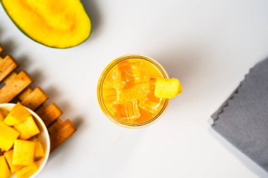 Bir bardak mango suyu ya da bir dilim mango meyvesi ve beyaz arka planda gri bir peçeteyle birlikte smoothie. Vitamin zengini içecek konseptleri