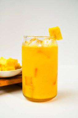 Arka planda taze mango meyvesi dilimi olan bir bardakta mango smoothie. Vitamin zengini ve sağlıklı beslenme kavramı.