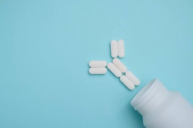 Beyaz kapsüller açık beyaz bir şişeden dökülüyor Dan parlak mavi arka planda bir antikor oluşturdu..